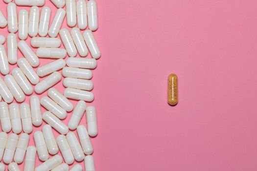 Top view of white pills on one side and a single brown pill on the other side on pink background with copy space. Healthcare, medical and pharmaceutical concept.