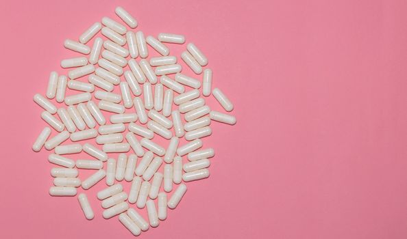 Top view of white pills on pink background with copy space. Healthcare, medical and pharmaceutical concept.