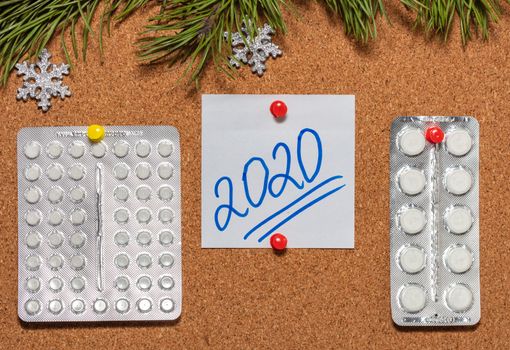 White pills, white sticky note with 2020 pinned on notice board which is decorated with pine twigs and snowflakes. Healthcare, christmas, new years celebration, new normal concepts. Close up shot