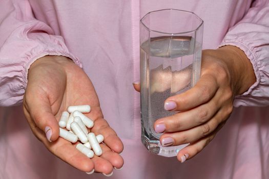 High angle closeup shot of female hands holding a bunch of white pills and a glass of water. Healthcare, medical and pharmaceutical concept.