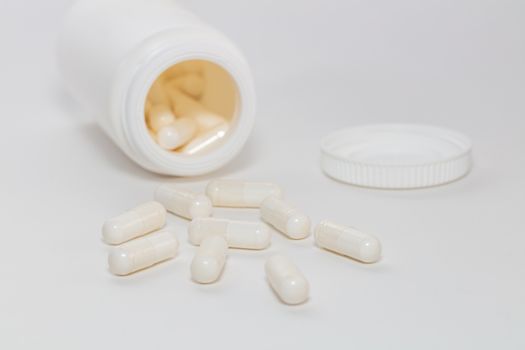Bunch of white scattered pills on white background. White pills container and cap next to them slightly out of focus in the background. Close up. Pharmaceutical business and medicine sale concepts.