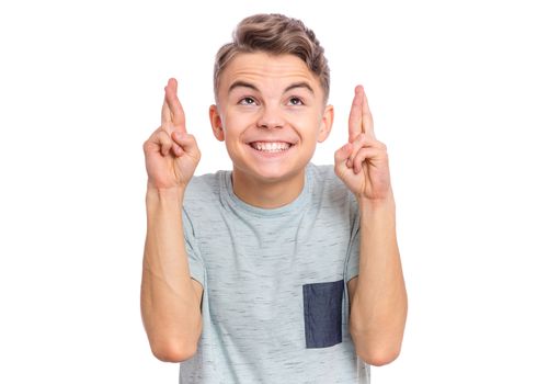 Handsome teen boy looking very happy holding fingers crossed for good luck, isolated on white background