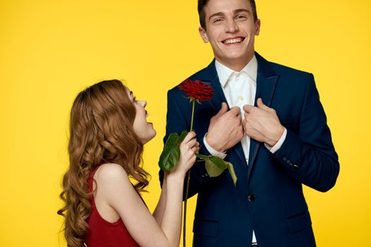 A romantic man hugs a woman in a red dress with a rose in his hand on a yellow background. High quality photo