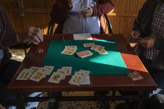 Luesia, Spain - October 12, 2020: A group of pensioners, wearing protective face masks, play cards in the afternoon, betting money, in a bar in the small town of Luesia, in the Cinco Villas region, Zaragoza.