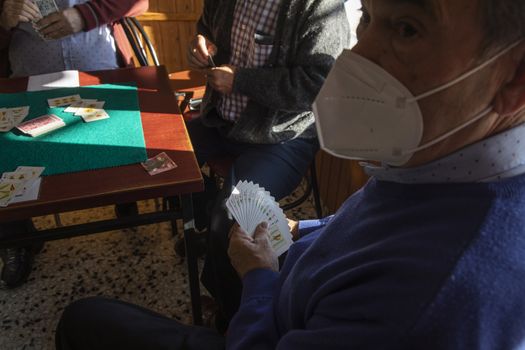 Luesia, Spain - October 12, 2020: A group of pensioners, wearing protective face masks, play cards in the afternoon, betting money, in a bar in the small town of Luesia, in the Cinco Villas region, Zaragoza.