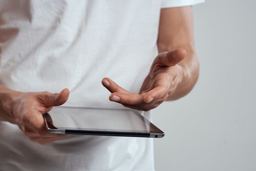 Tablet with a touch screen on a light background male hands white t-shirt cropped view. High quality photo