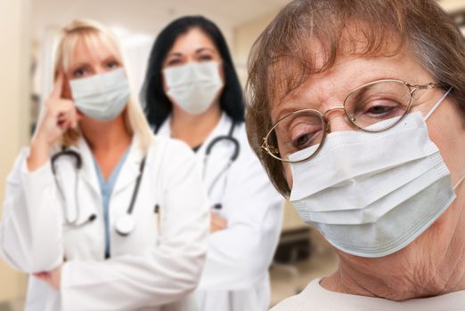 Senior Adult Female Looking Down as Doctors stand Behind All Wearing Medical Face Masks.