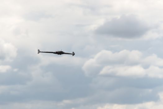 Gentle fluffy clouds in a grey sky form the background behind this FPV first person view flying wing drone. Selective focus and head on view.