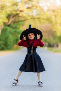 Little girl in a witch costume stands on the road on a halloween party in the village