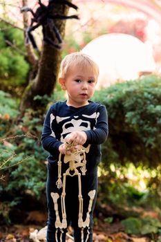 Little boy in a skeleton costume holding a skeleton on a halloween party in the garden