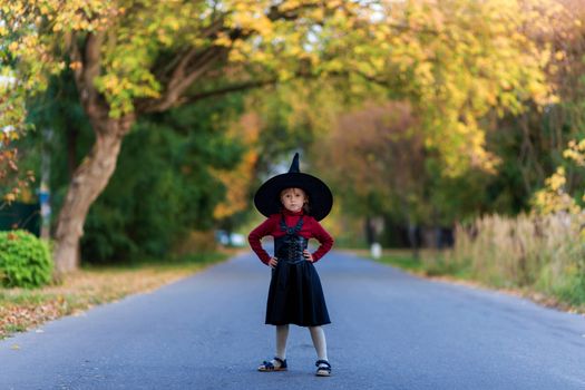 Little girl in a witch costume stands on the road on a halloween party in the village