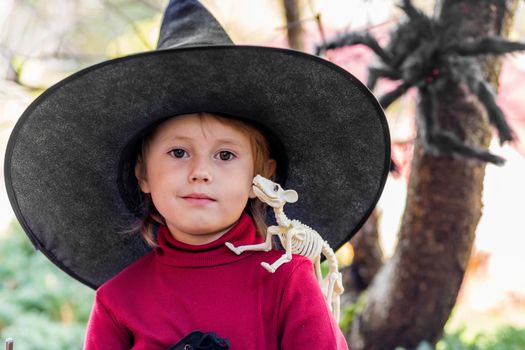 Little girl in witch costume making different faces on halloween party in the garden