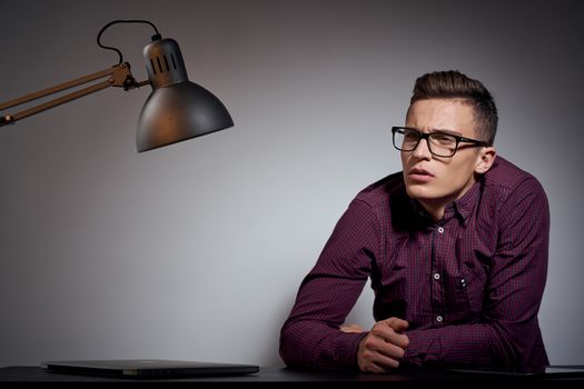 business man with glasses and a shirt sitting at a table in a dark room with a lamp cropped view. High quality photo