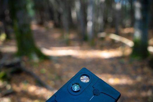A tiny compass embedded in a credit-card-shaped multi-tool is held up in the woods.