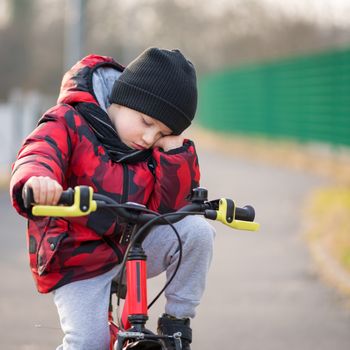 Sad, angry boy with hat and scarf sitting on bicycle at park.