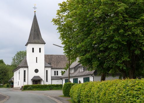 View along the central street of the Sauerland village Westfeld with parish church, old buildings and tree, Schmallenberg, Germany