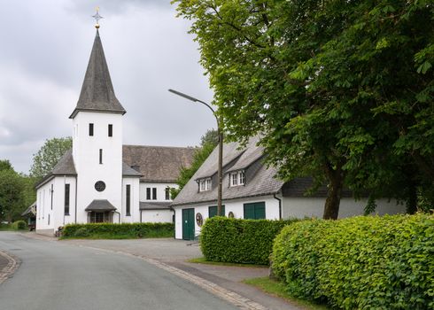 View along the central street of the Sauerland village Westfeld with parish church, old buildings and tree, Schmallenberg, Germany