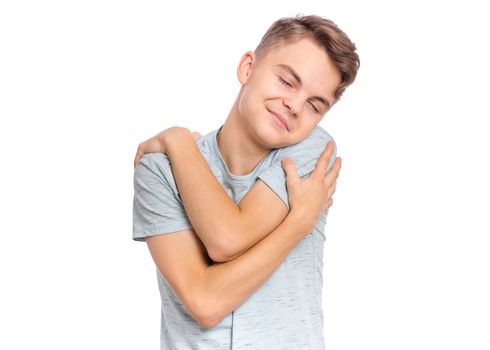 Handsome teen boy with closed eyes hugs himself, isolated on white background