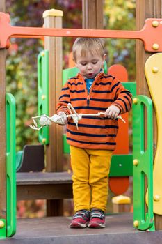 A small child in a striped sweater holds a skeleton toy in his hands and rides down a slide on the playground