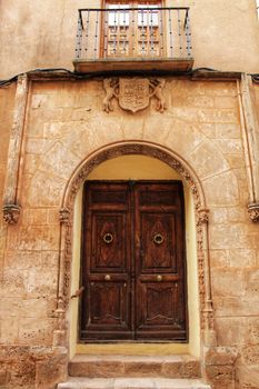 Old stone facade made of carved stone and vintage wooden door in a majestic house in Alcaraz, Albacete province, Spain.