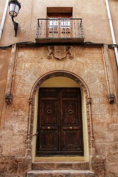 Old stone facade made of carved stone and vintage wooden door in a majestic house in Alcaraz, Albacete province, Spain.