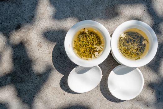 Two white cups of tea top view on a grey stone table in sunlight under a tree in Chengdu, Sichuan province, China