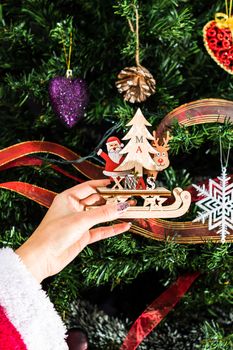 Hands holding Christmas ornament in front of Christmas tree. Decorating fir branches with Christmas decorations.