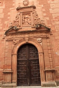 Old stone facade made of carved stone and vintage wooden door in a majestic house in Villanueva de los Infantes, Ciudad Real community, Spain. Encarnacion convent facade.