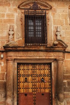 Old stone facade made of carved stone and vintage wooden door in a majestic house in Villanueva de los Infantes, Ciudad Real community, Spain