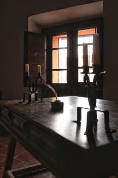 Antique wooden desk with chandeliers and open window in the background