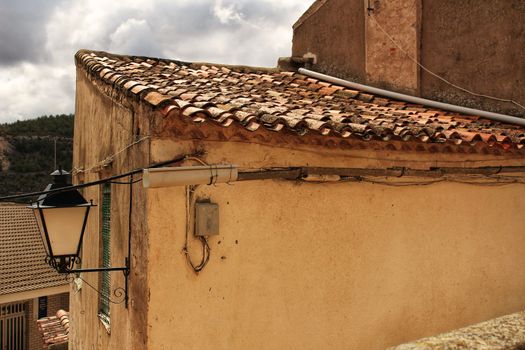 Old roof of stone house in Jorquera village. Mountains in the background. Lantern on the facade.