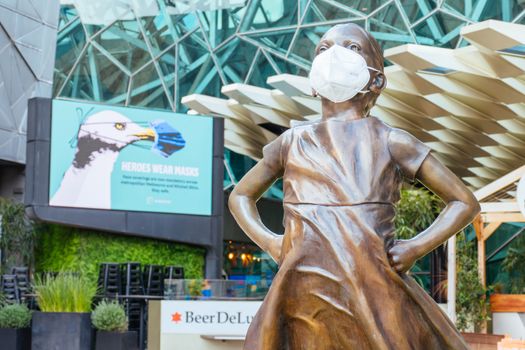 Melbourne, Australia - October 10th 2020: Federation Square and a masked statue of Fearless Girl in Melbourne is quiet and empty during the Coronavirus pandemic and associated lockdown.