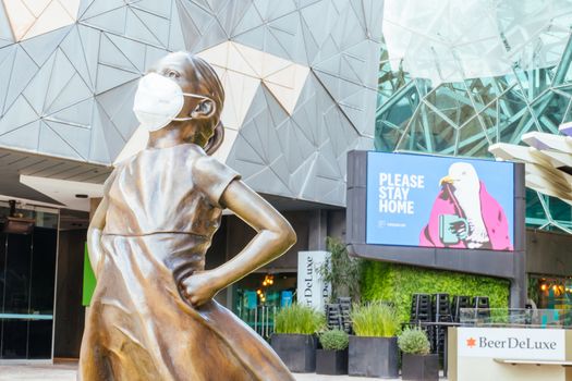 Melbourne, Australia - October 10th 2020: Federation Square and a masked statue of Fearless Girl in Melbourne is quiet and empty during the Coronavirus pandemic and associated lockdown.