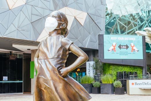 Melbourne, Australia - October 10th 2020: Federation Square and a masked statue of Fearless Girl in Melbourne is quiet and empty during the Coronavirus pandemic and associated lockdown.