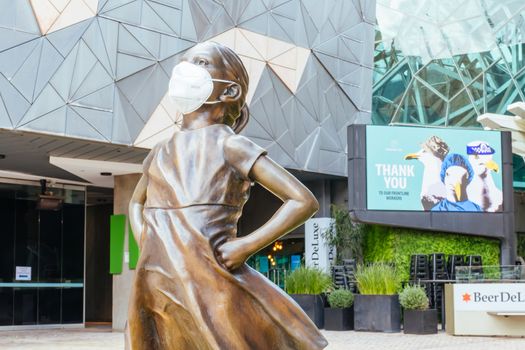 Melbourne, Australia - October 10th 2020: Federation Square and a masked statue of Fearless Girl in Melbourne is quiet and empty during the Coronavirus pandemic and associated lockdown.