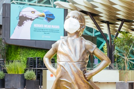 Melbourne, Australia - October 10th 2020: Federation Square and a masked statue of Fearless Girl in Melbourne is quiet and empty during the Coronavirus pandemic and associated lockdown.