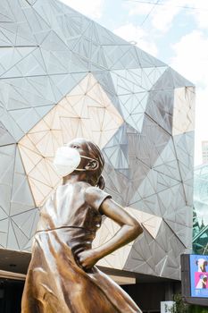 Melbourne, Australia - October 10th 2020: Federation Square and a masked statue of Fearless Girl in Melbourne is quiet and empty during the Coronavirus pandemic and associated lockdown.