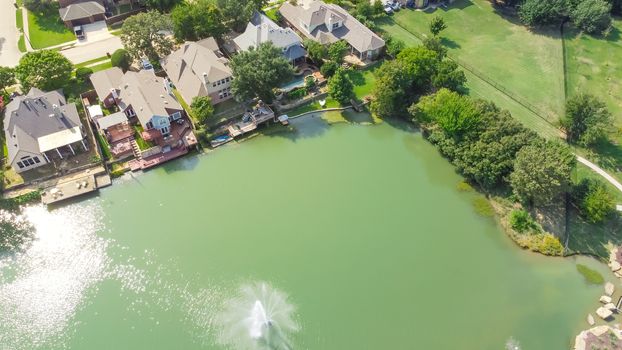 Aerial view upscale lakeside and park side houses with water fountain in Flower Mound, Texas, USA. Row of two story waterfront homes with private docking, swimming pools. Wealthy residential area