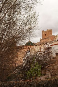 Beautiful overview of the town of Alcala de Jucar with the fortress castle and the church in spring under gray sky