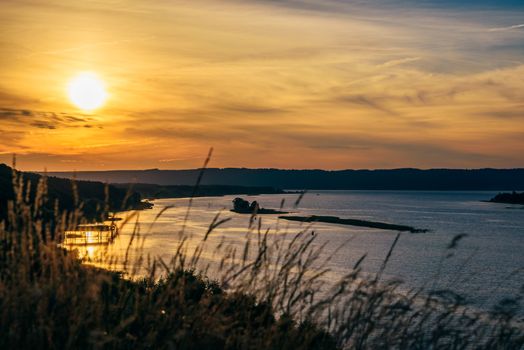 Grass against the river shore in the sunset light. Blurred foreground.