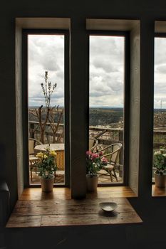 Mountains view under gray sky through the window in spring. Wooden table and pots in the foreground