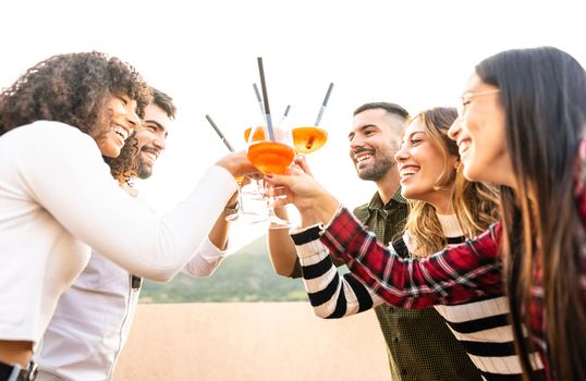 Mixed race happy friends group toasting with spritz glasses outdoor at sunset - Young people having fun together drinking cocktail for aperitif time - Bright vivid filter with focus on bearded men