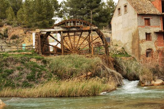 Old wooden Waterwheel and Cabriel River on its way through Casas del Rio village, Albacete, Spain. Landscape between cane field and mountains.