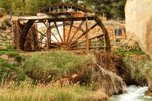 Old wooden Waterwheel and Cabriel River on its way through Casas del Rio village, Albacete, Spain. Landscape between cane field and mountains.