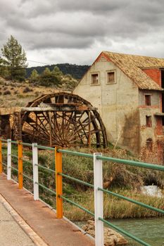 Old wooden Waterwheel and Cabriel River on its way through Casas del Rio village, Albacete, Spain. Landscape between cane field and mountains.