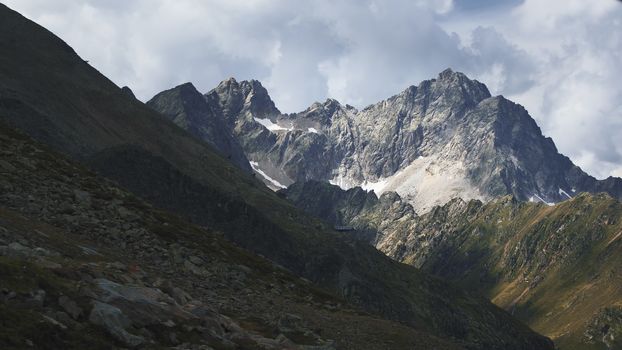 Aerial shot of the high mountains of the Austrian Alps in Kuhtai during summer season. The sunshine illuminates the beautiful landscape.