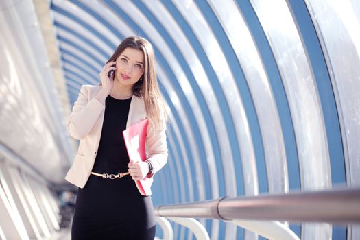 Young Businesswoman with folder talking on the phone in modern building