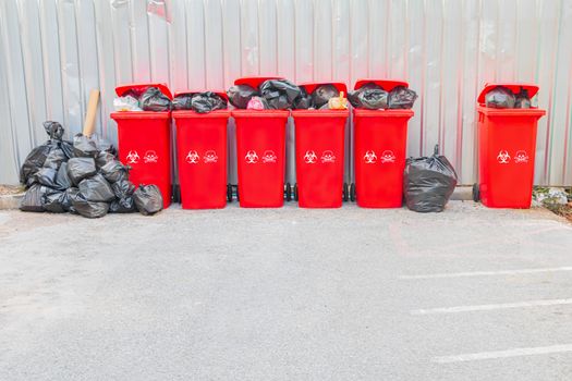 group red bins six with symbol infectious and  garbage bag black pile On top in the outdoors. concept prevent infection coronavirus (covid-19)