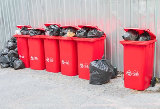 group red bins six with symbol infectious and  garbage bag black pile On top in the outdoors. concept prevent infection coronavirus (covid-19)