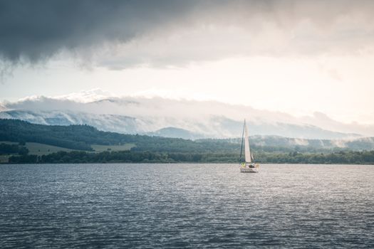 Sailing boat floats on the lake with stormy clouds sky. Autumn sailboat ship water sport scene from Lipno